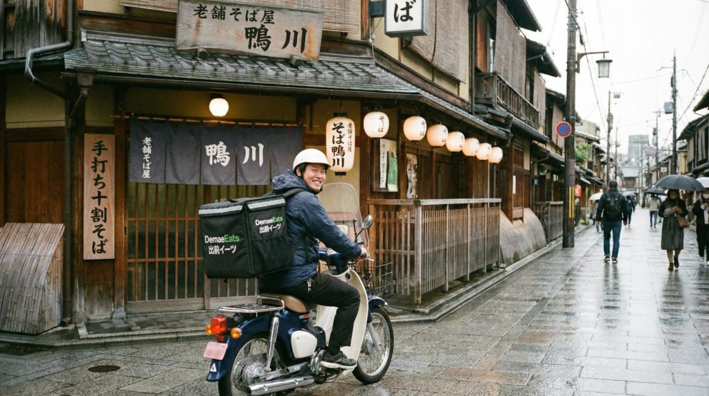 料理をバイクで運ぶフードデリバリー配達員